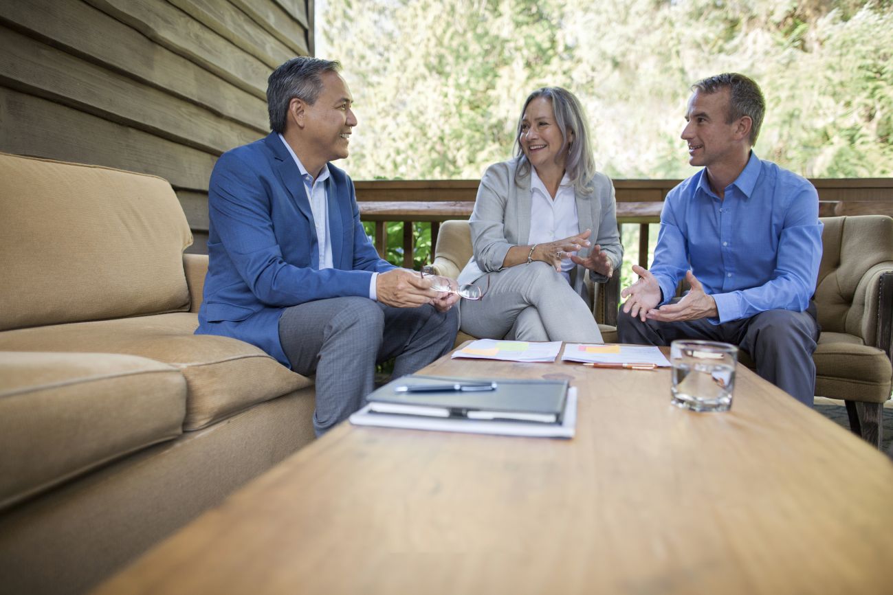 two men and a woman talking around a table with trees in the background