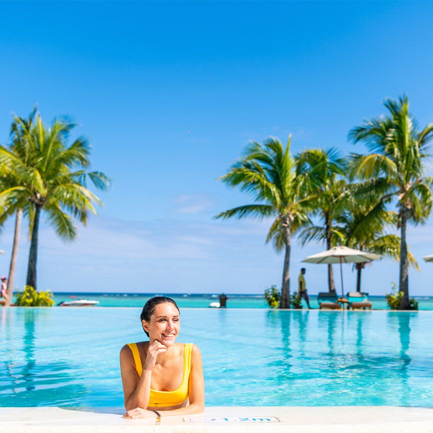 woman smiling in a swimming pool surrounded by palm trees