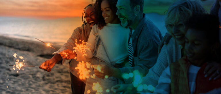 three people on beach at sunset with sparklers